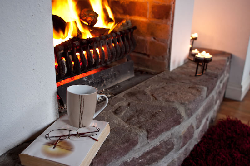 View of open turf fire at Achill Cottages, shown with reading book, glasses and cup of tea